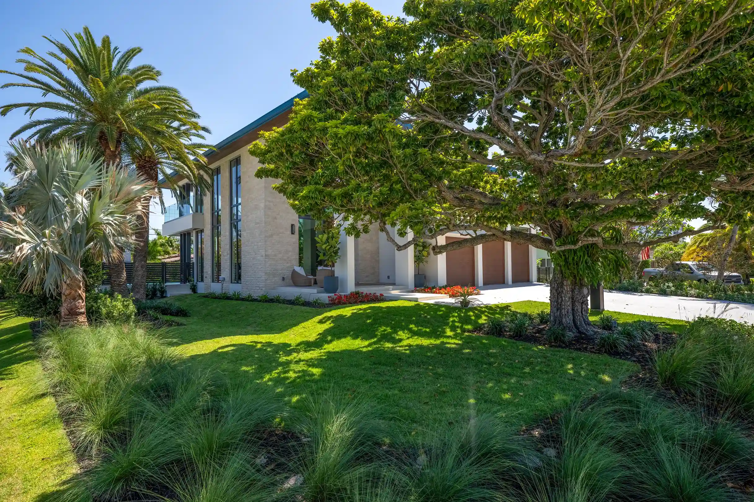 Street view of a modern luxury residence surrounded by mature trees and tropical landscaping.
