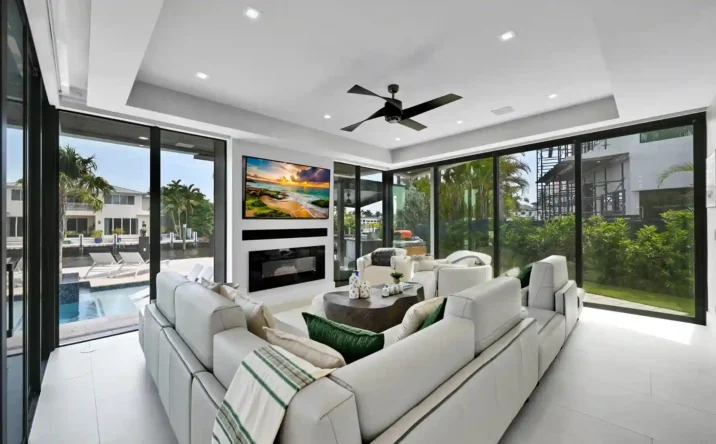 Open-concept living room with floor-to-ceiling windows overlooking the waterfront and tropical scenery.