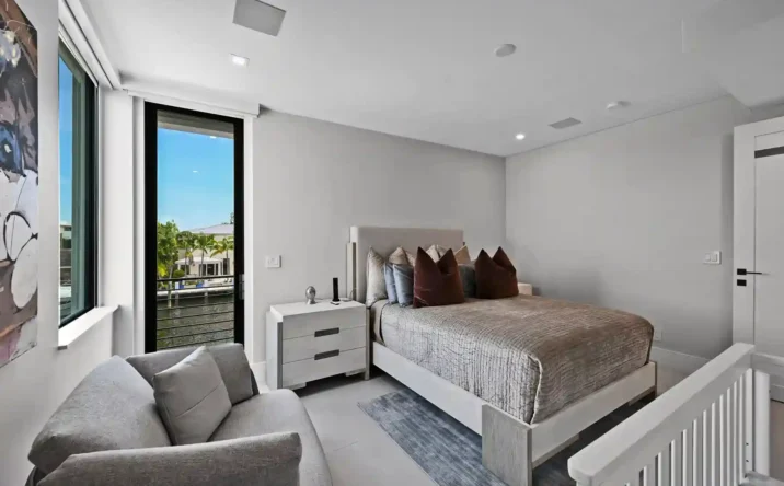 Bright modern bedroom with large windows, neutral décor, and waterfront views.