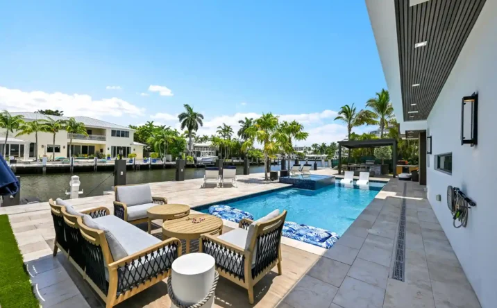 Luxury waterfront patio overlooking a private canal with palm trees and neighboring modern homes.