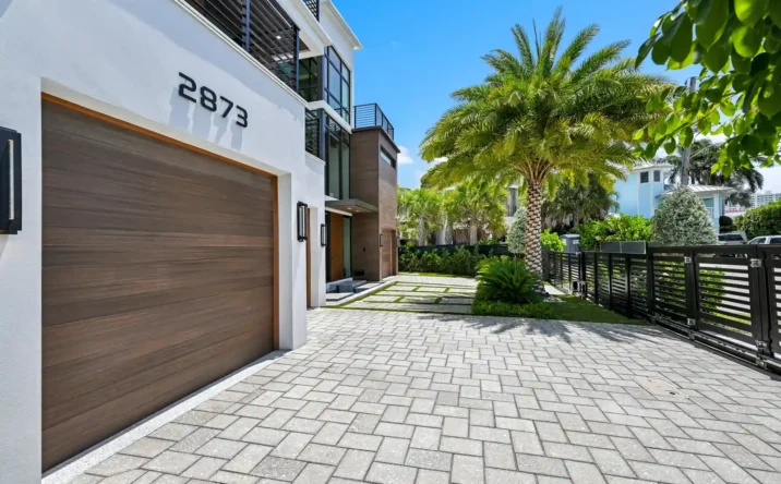 Contemporary front entrance with wood accents, large windows, and lush tropical landscaping.