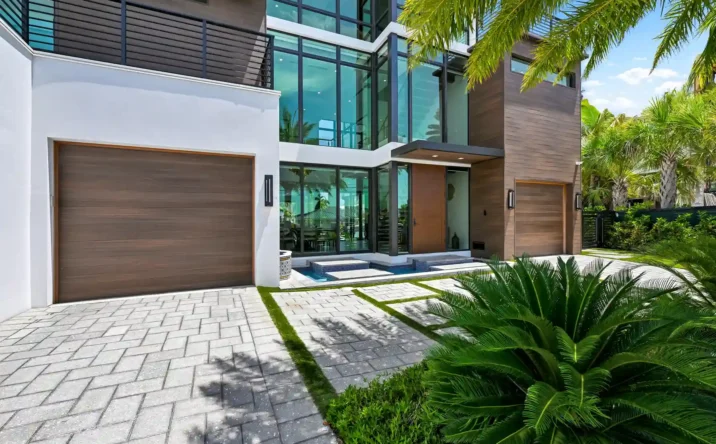 Close-up of a modern luxury home's front entrance with wood accents, glass walls, and tropical landscaping.