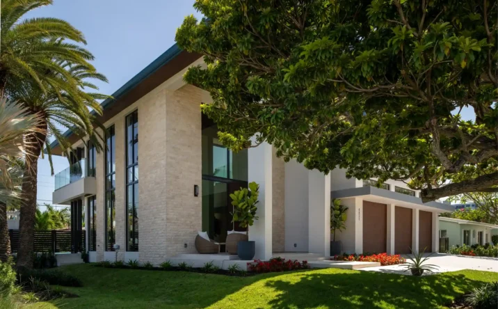 Luxury modern home featuring stone façade, large windows, and mature shade trees.