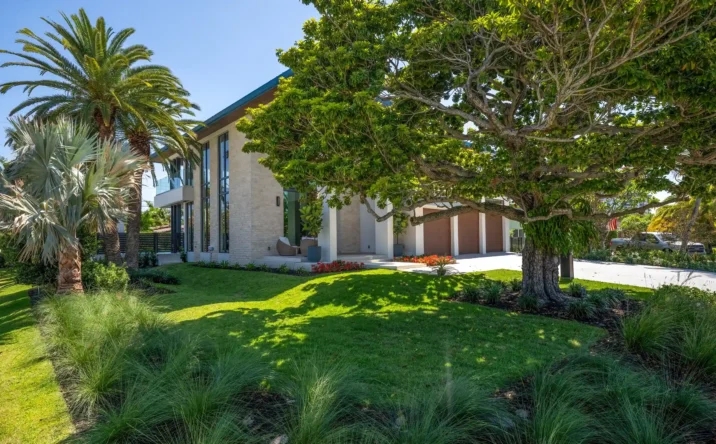 Street view of a modern luxury residence surrounded by mature trees and tropical landscaping.